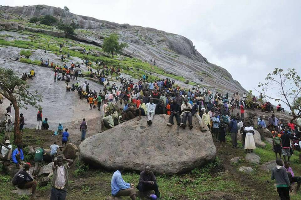 Large crowd of pilgrims or tourists climbing the steep, rocky slopes of Kagulu Hill in the Busoga region of Uganda.