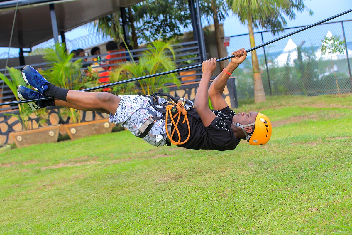 Tourist secured in a harness on a low-ropes course obstacle at an Extreme Adventure Park in Uganda, showcasing the popular team building and outdoor activities